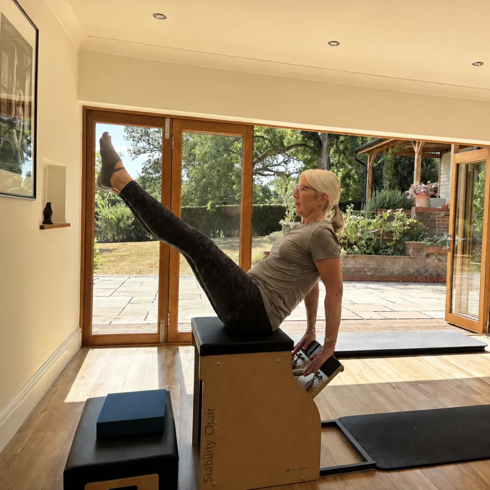 A client balanced along the Stability Chair with one leg raised, the studio’s garden doors open behind her