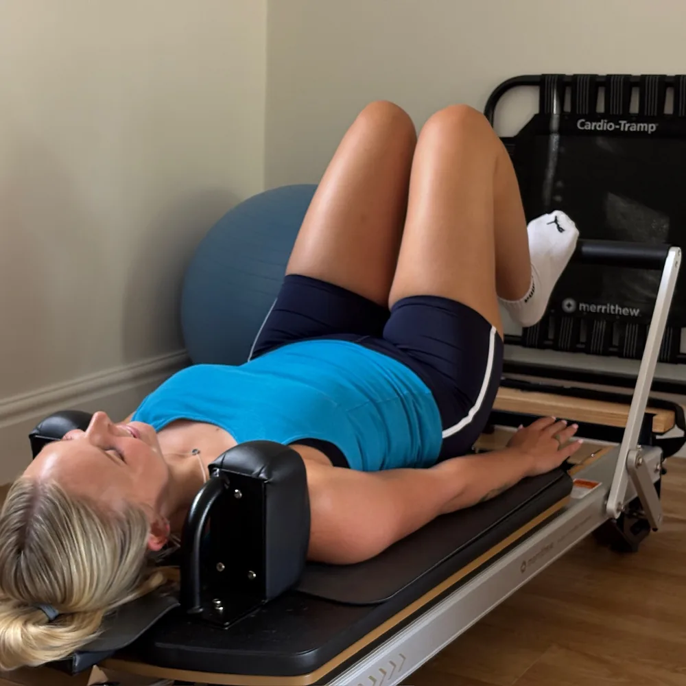 A client lying back on the Reformer carriage, knees bent and feet resting on the jump board at the far end