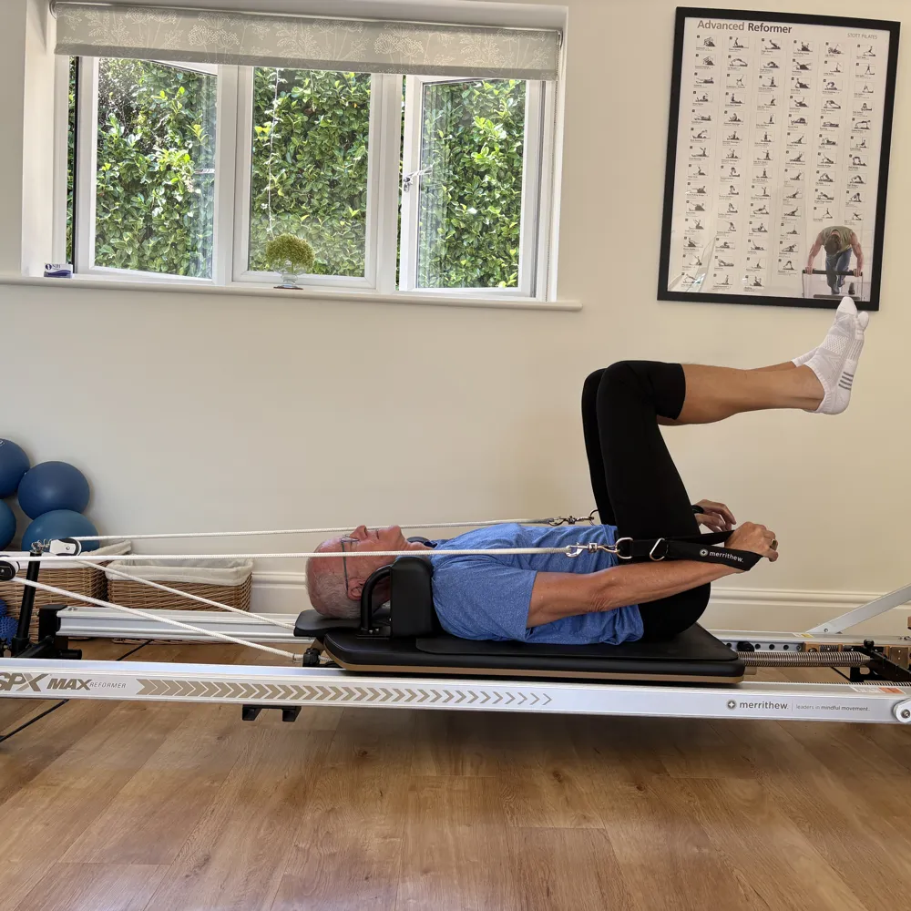 A client lying on the Reformer with knees folded to tabletop, holding the straps in both hands