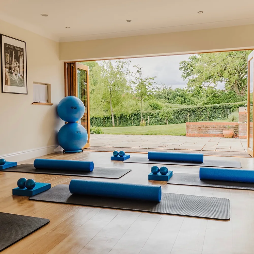 The studio laid out for a mat class, a roller and a pair of weighted balls on each mat, with the garden doors folded open at the far end