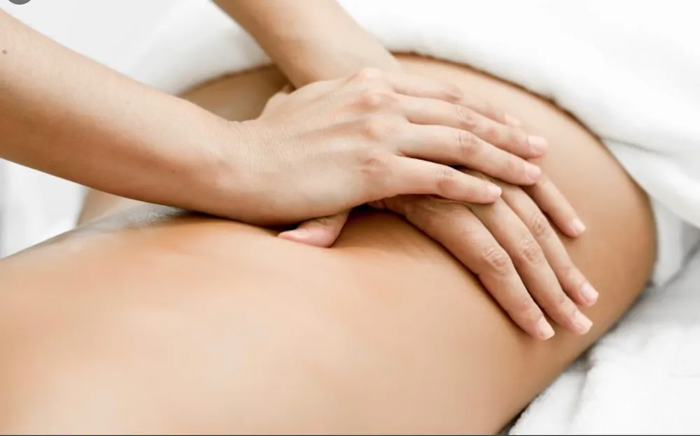 One hand stacked over the other, pressing along the length of a client’s back on the treatment couch